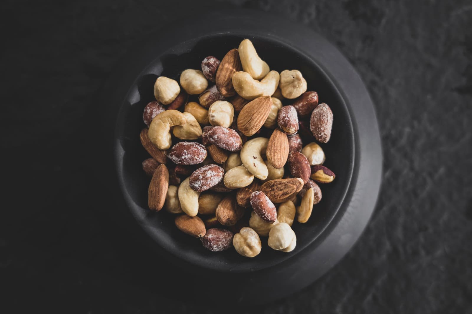 Mixed almonds, cashews and hazelnuts in a dark bowl