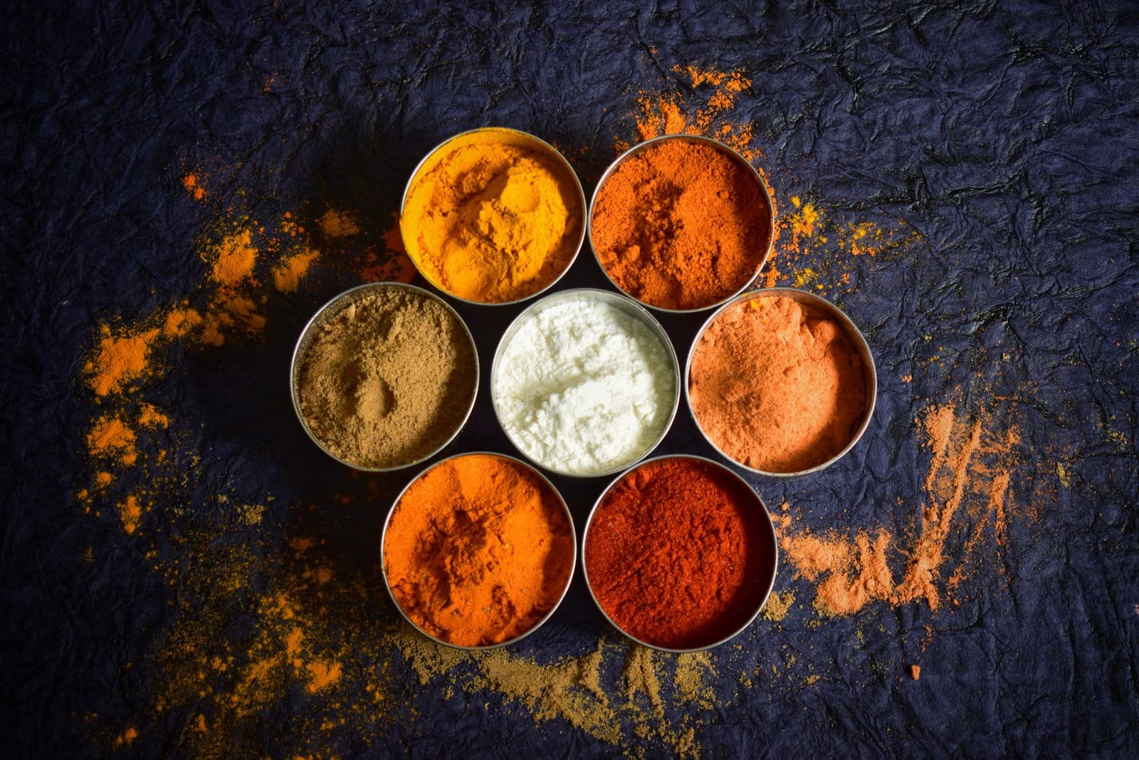 Ground turmeric, chilli and other spices in metal bowls on a dark surface